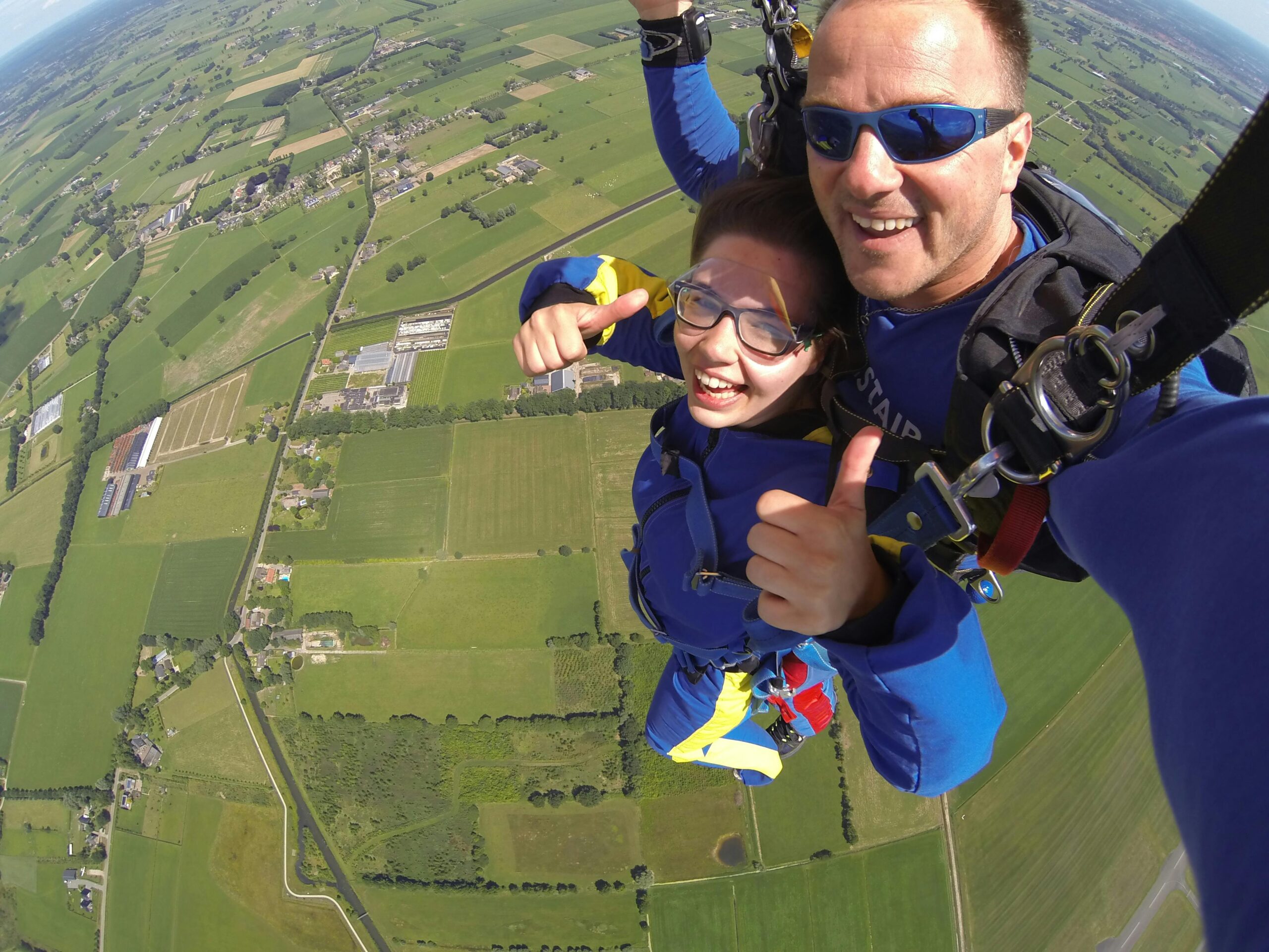 Thrilling tandem skydive with two people enjoying the aerial view of lush green fields.
